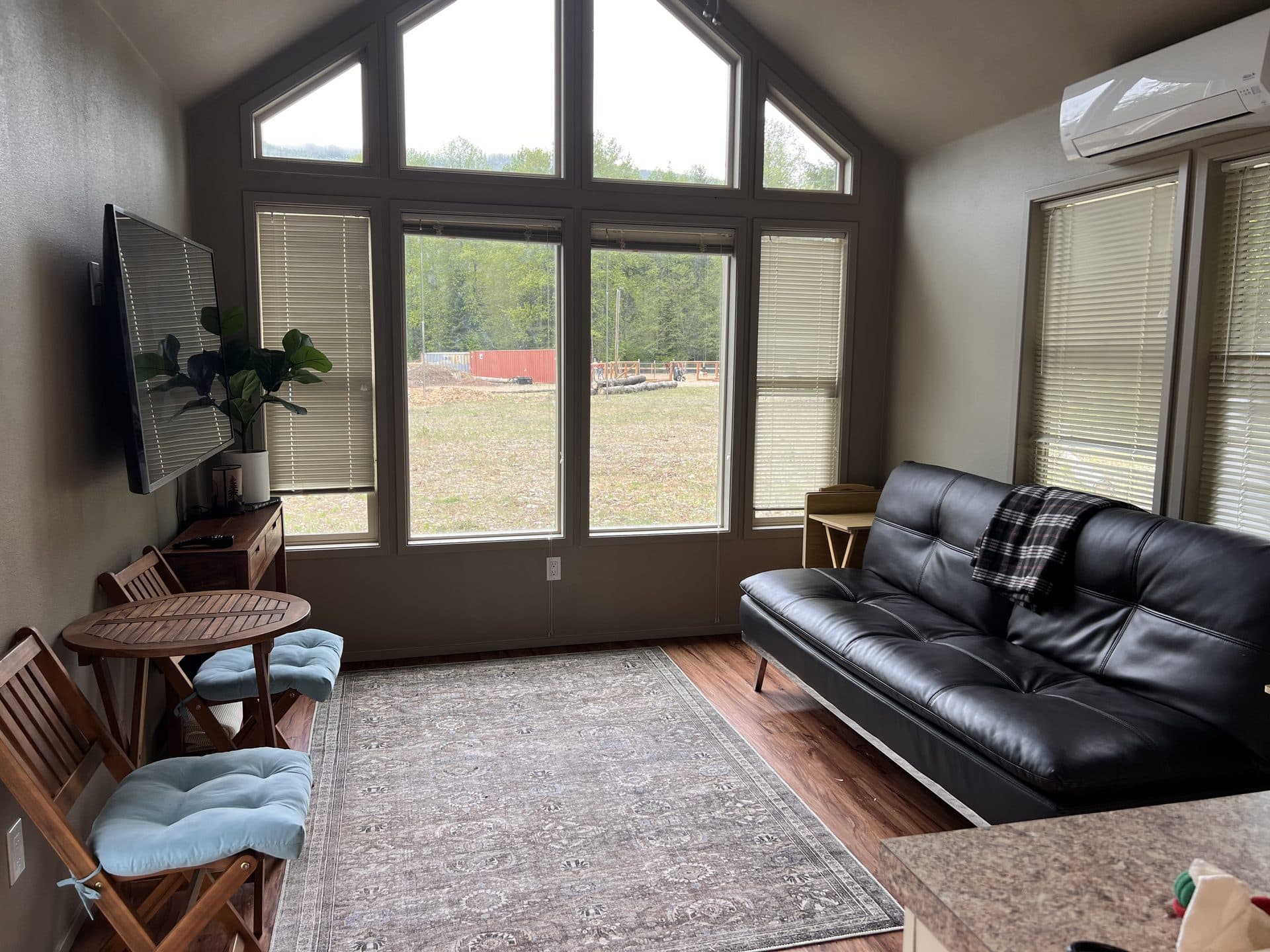 Tiny home interior with floor-to-ceiling A-frame windows looking out at evergreens